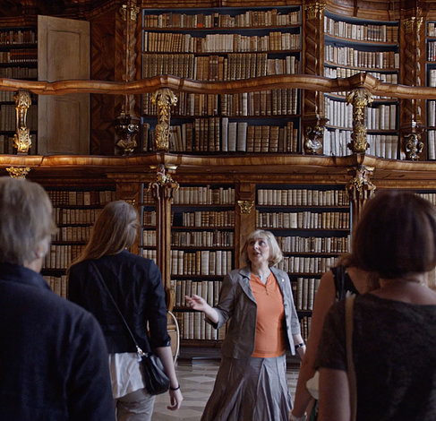 A tour guide is presenting the historical provincial library to guests in Neuburg on the danube. In the background you can see the rich rococo bookshelves.